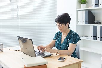 Business, people and technology concept - middle-aged woman with laptop computer working at home or office
